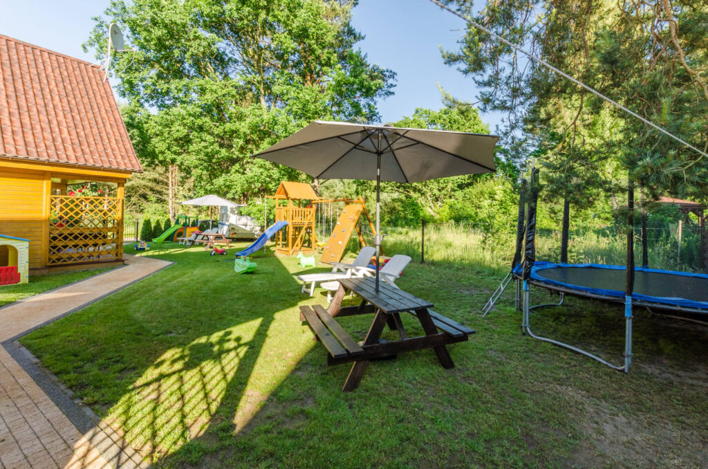 Ogród przy domkach z trampoliną, placem zabaw i stołem pod parasolem