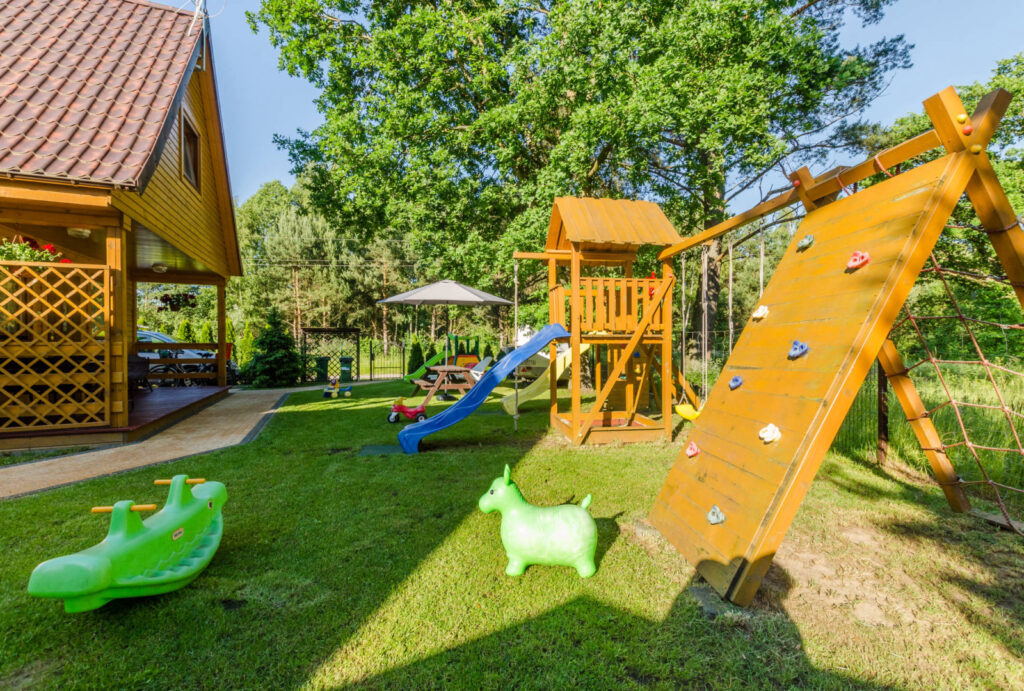 Drewniany plac zabaw ze zjeżdżalnią i ścianką wspinaczkową w ogrodzie