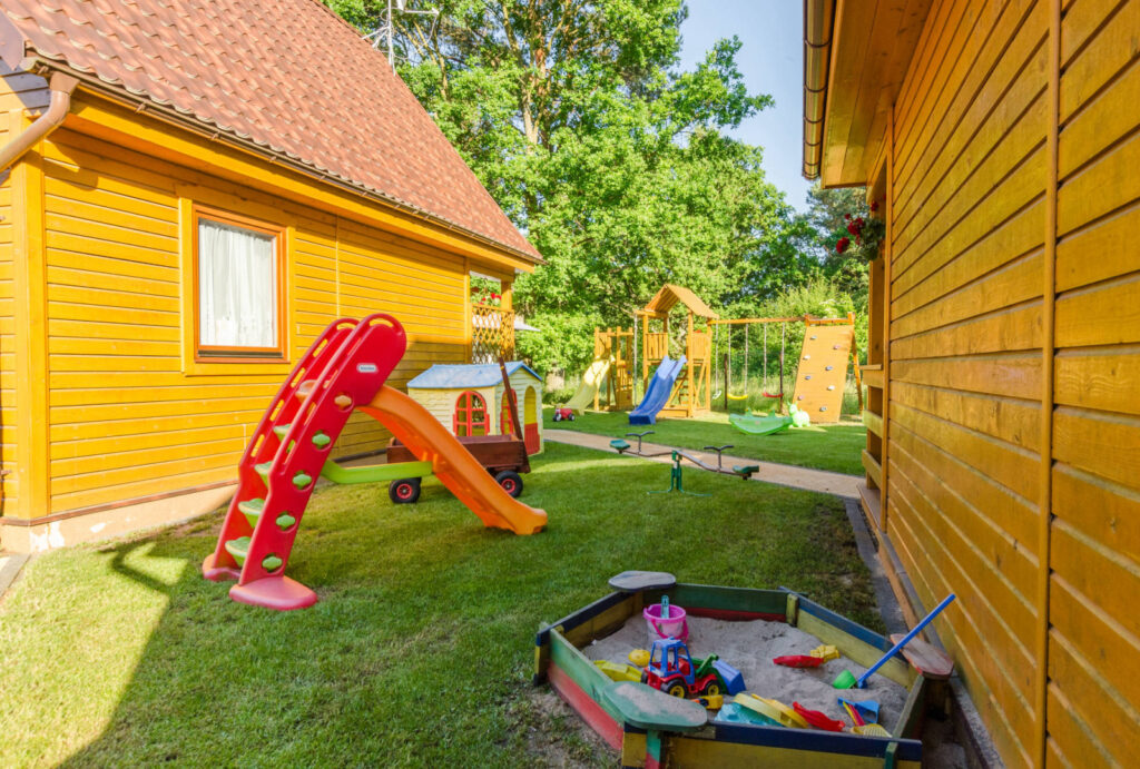 Piaskownica i dziecięca zjeżdżalnia pomiędzy drewnianymi domkami